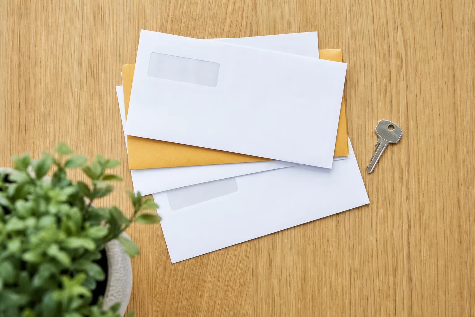 Blank household bill envelopes and a house key arranged on a bright white counter.