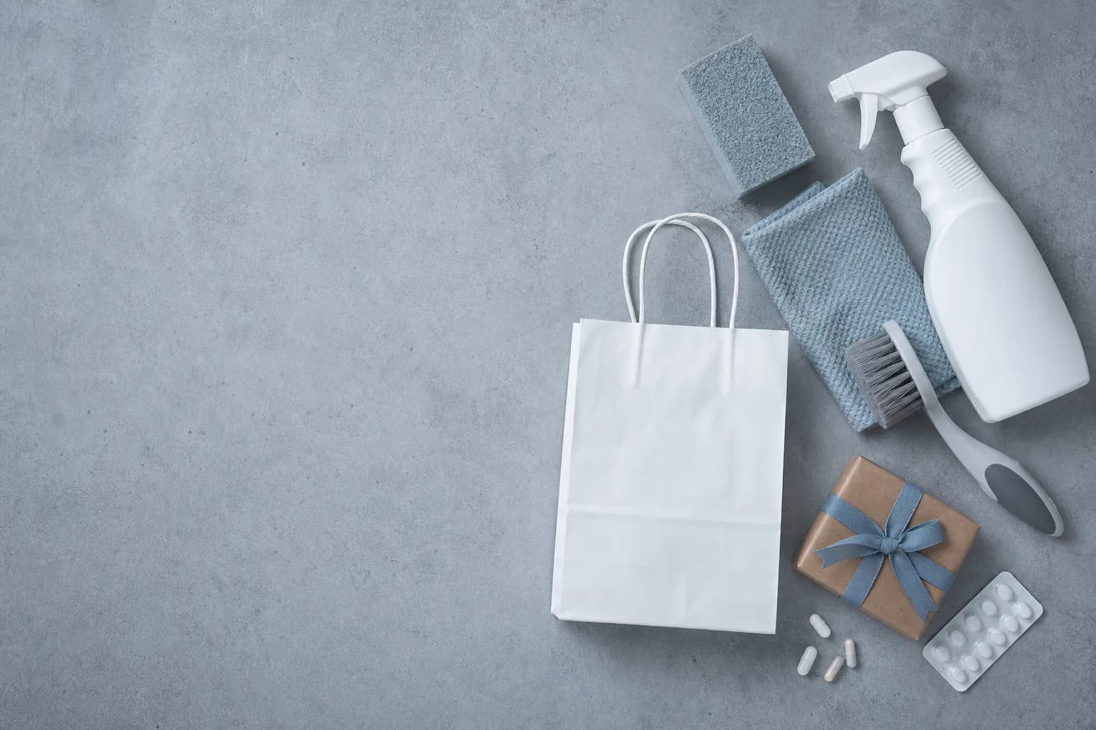 An unbranded pharmacy bag, household cleaning supplies, and a small wrapped gift arranged on the right side of a tabletop.