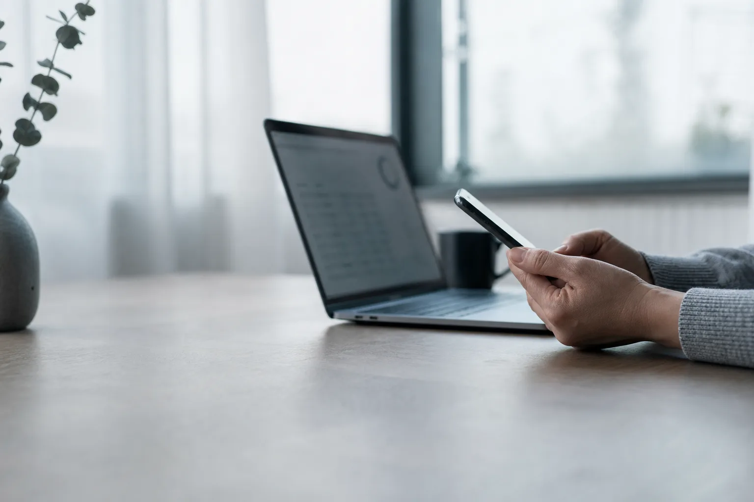 Hands use a smartphone beside a laptop during a quiet budgeting check-in at a table.