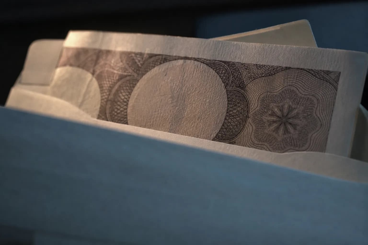 A banknote is carefully drawn from a plain savings envelope in a dim, warmly lit room.